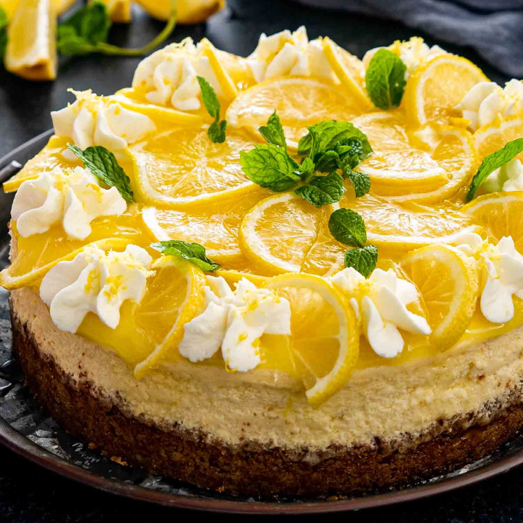 a freshly baked and beautifully decorated lemon cheesecake on a metal cake platter.