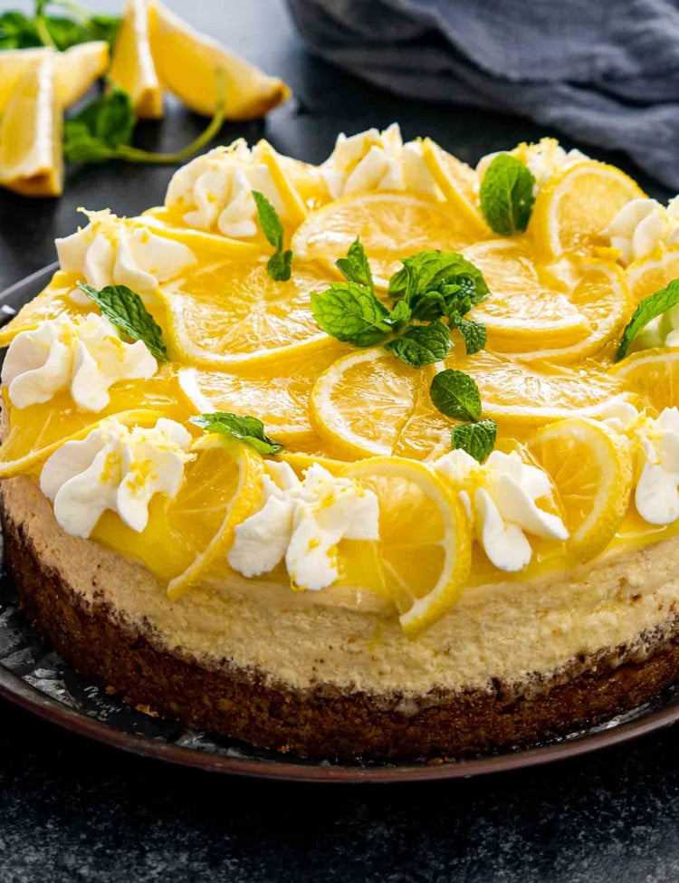a freshly baked and beautifully decorated lemon cheesecake on a metal cake platter.