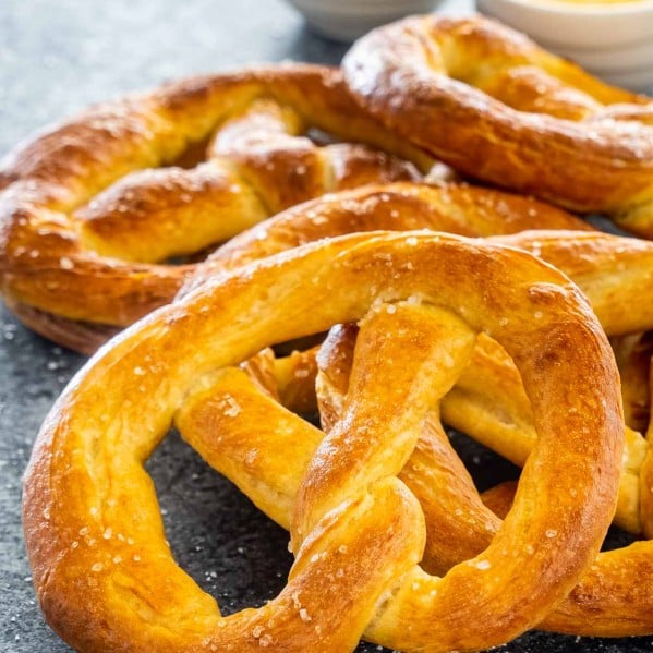 a bunch of soft pretzels stacked on top of each other with cheese sauce and mustard.