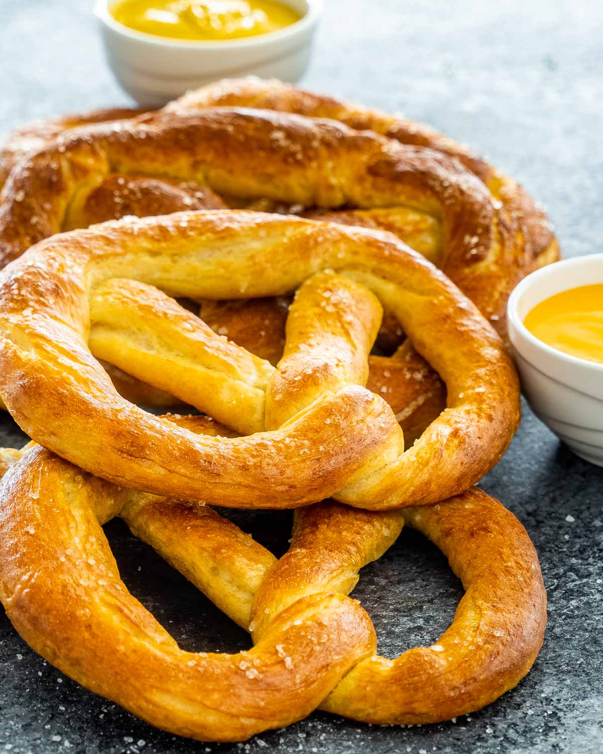 a bunch of soft pretzels stacked on top of each other with cheese sauce and mustard.