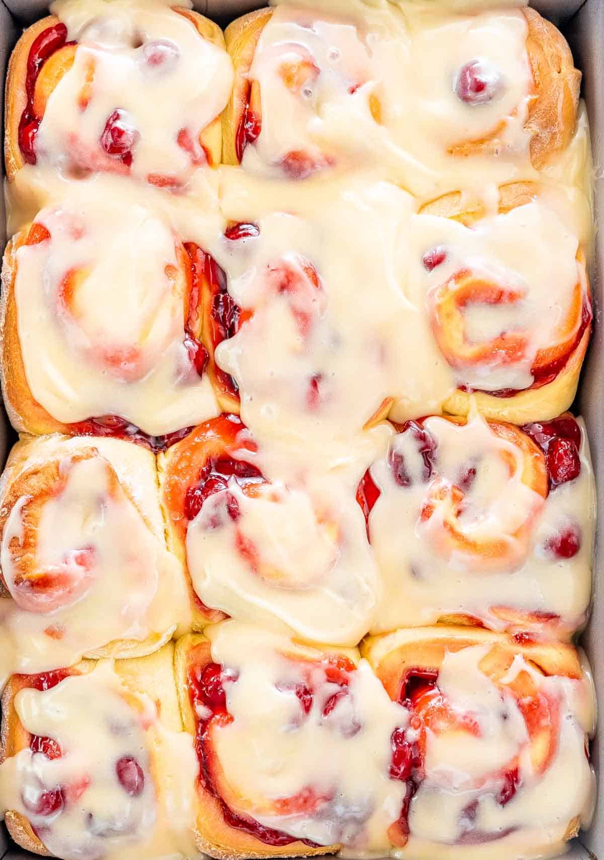 freshly baked cherry rolls with cream cheese icing in a baking pan.