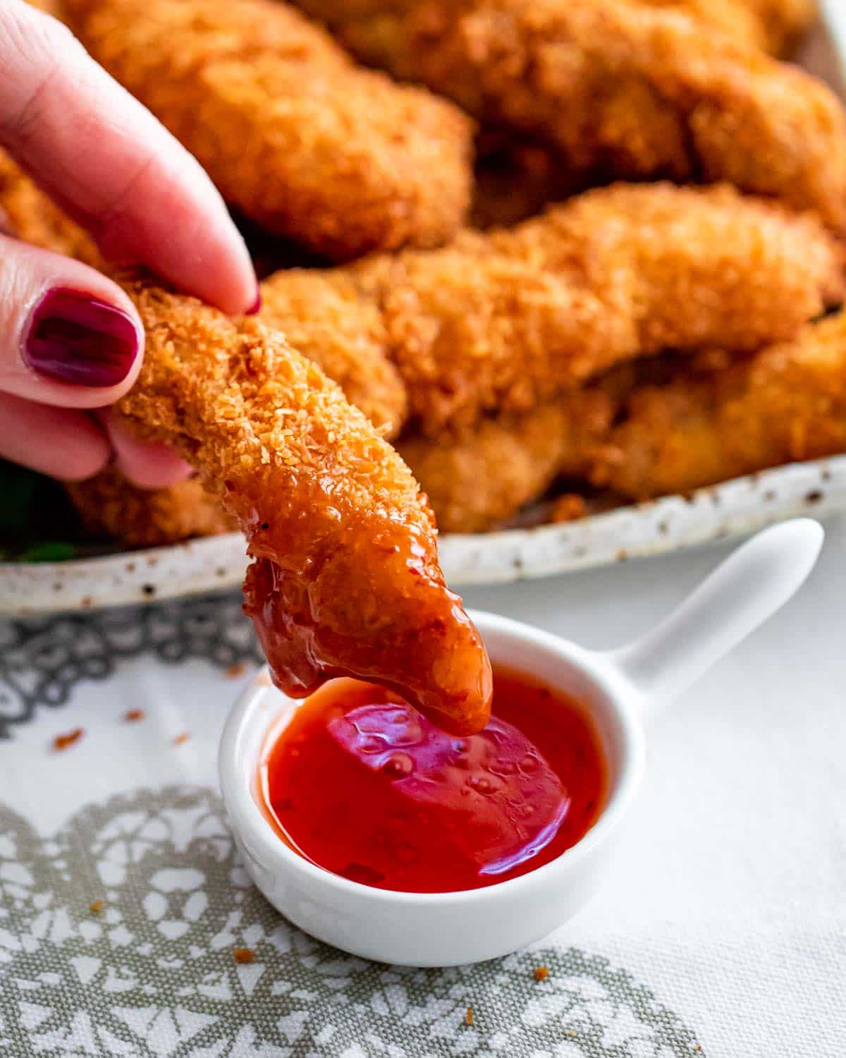 a hand dipping a coconut chicken piece in sweet and sour sauce.