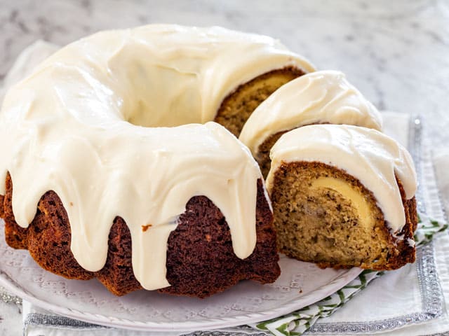 cutting into a banana cake covered in cream cheese icing
