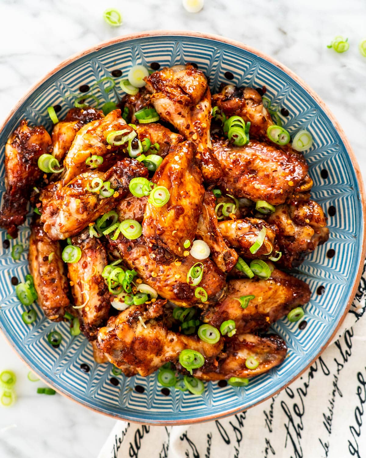 overhead shot of honey garlic chicken wings garnished with green onions in a blue plate
