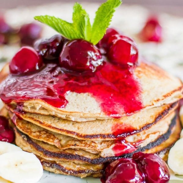 a stack of banana oatmeal pancakes topped with fresh cherry sauce