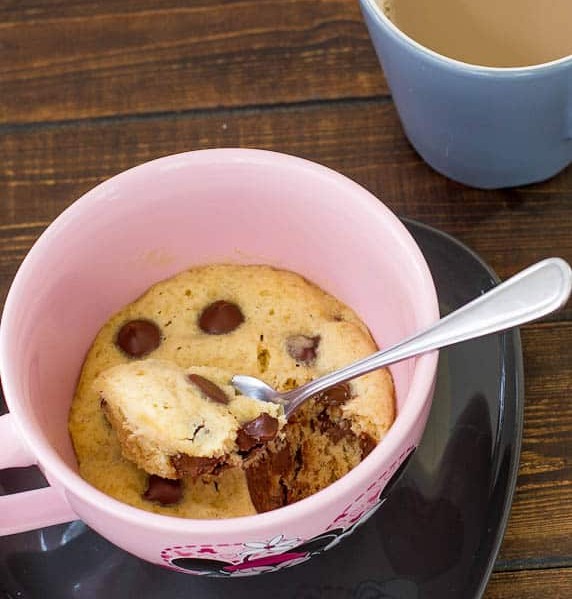 a spoon taking a bite of a chocolate chip cookie in a cup