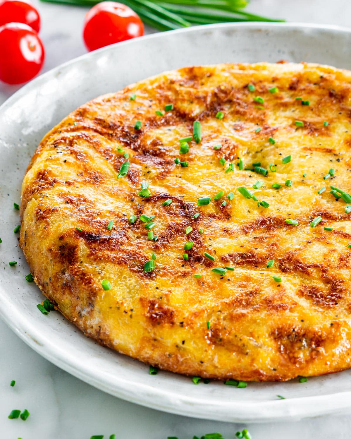 side view shot of a full spanish omelette on a grey plate garnished with chives