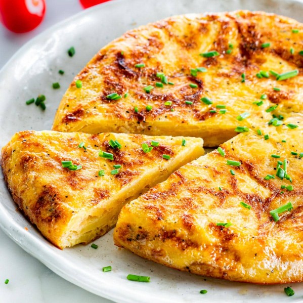 side view shot of spanish omelette on a plate with one slice cut out, and garnished with chives