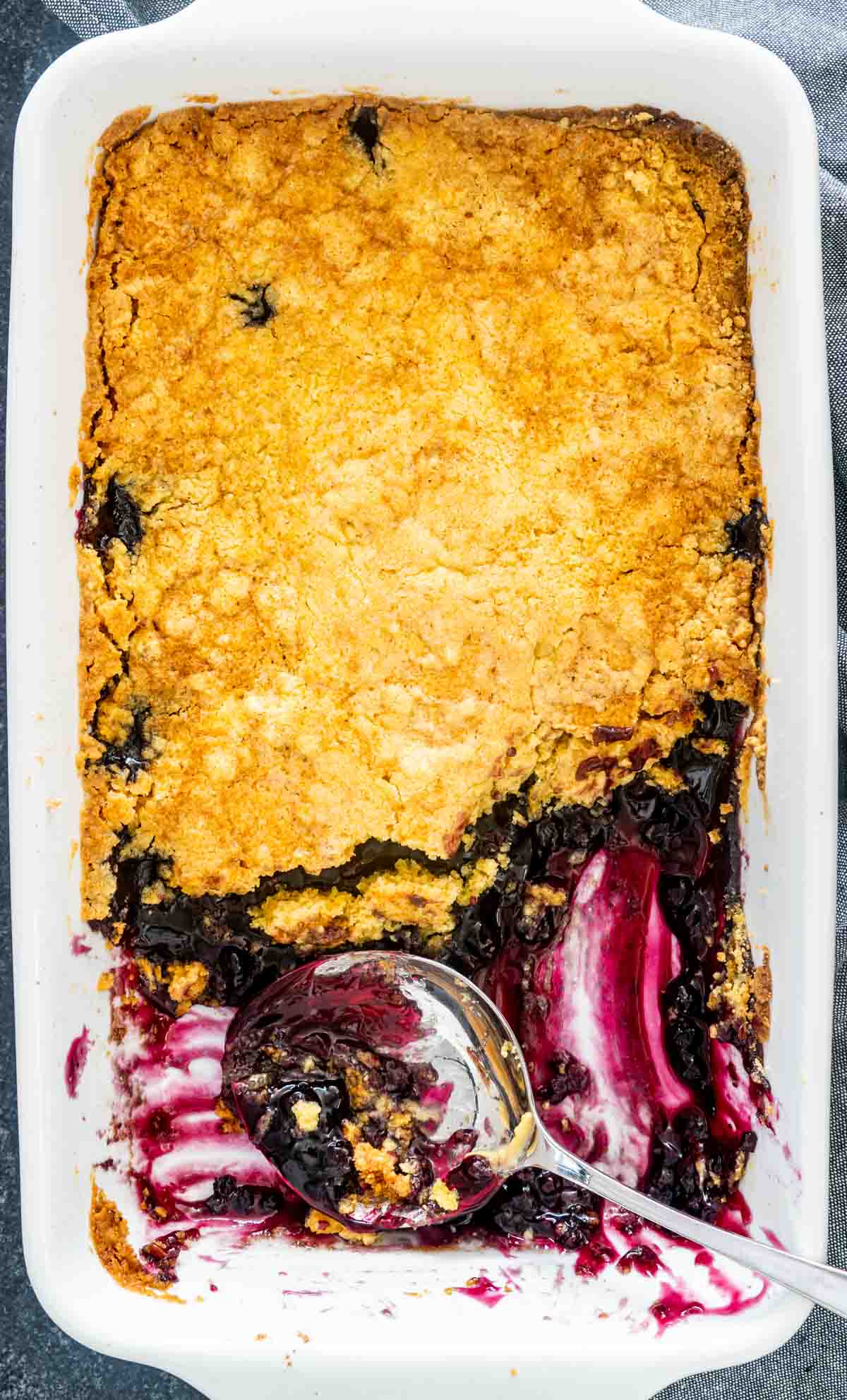 blueberry dump cake in a white baking dish with almost half of it out and a serving spoon in it.