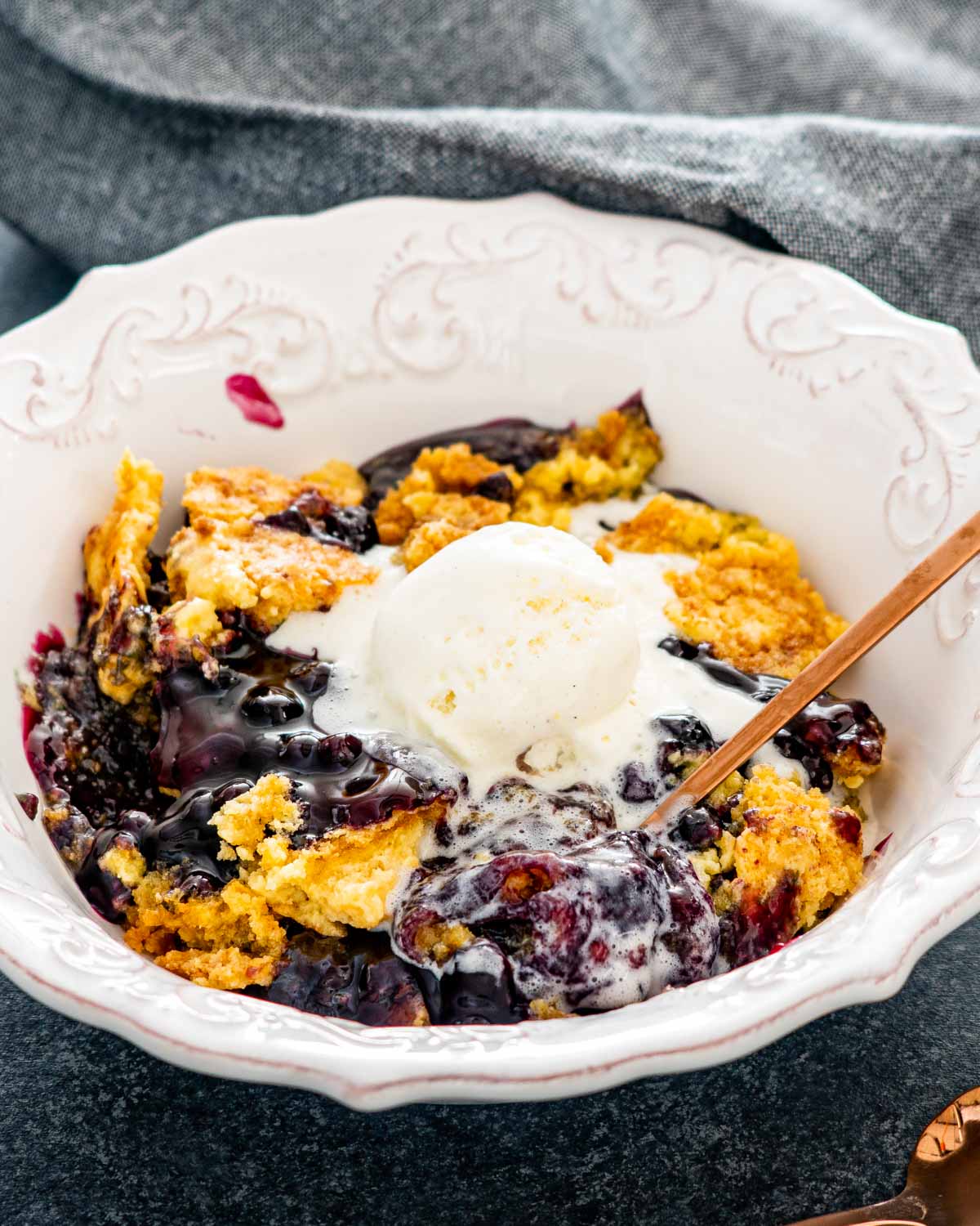 blueberry dump cake in a white bowl with a scoop of ice cream.