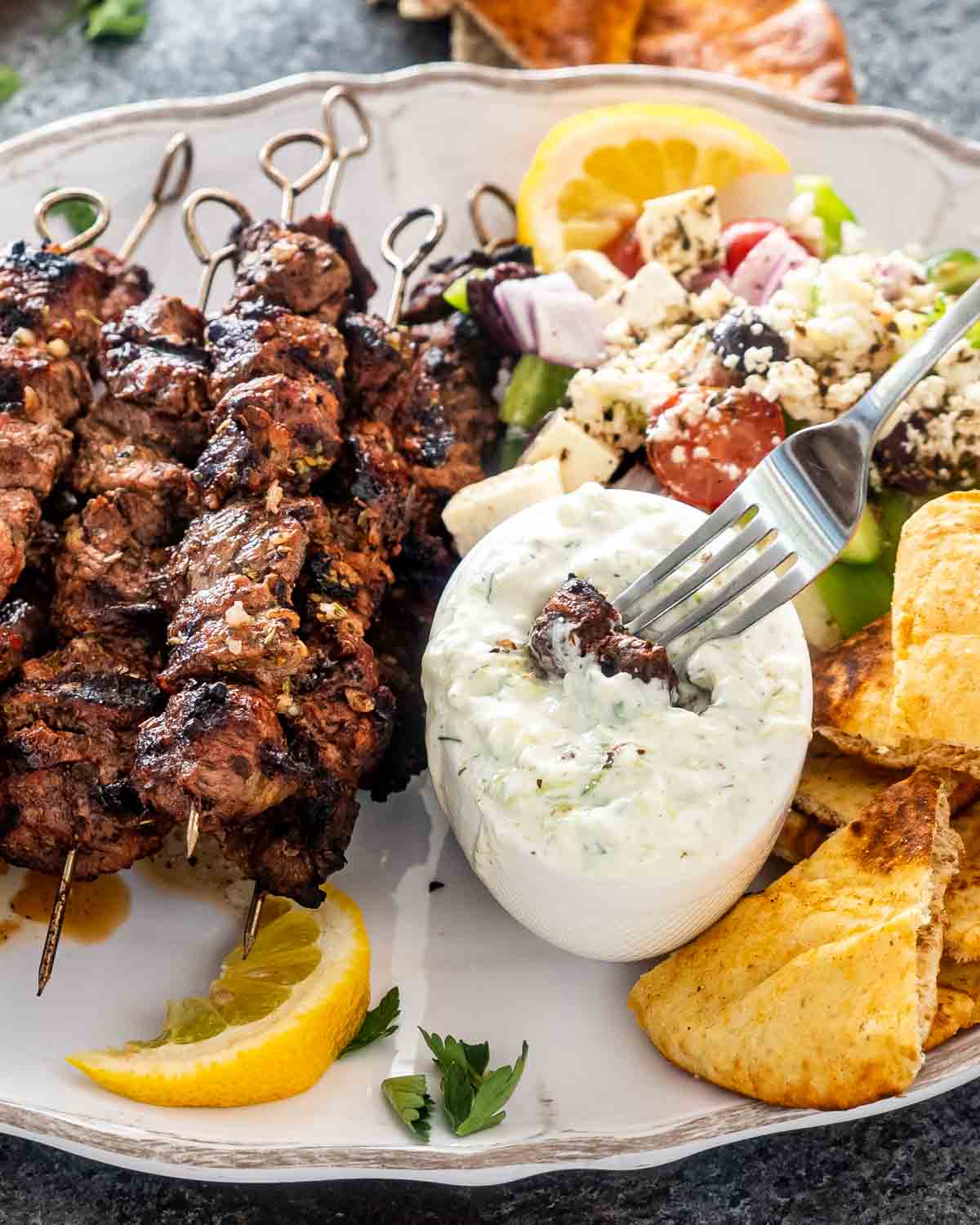 lamb souvlaki on a platter with tzatziki sauce, greek salad and pita bread.