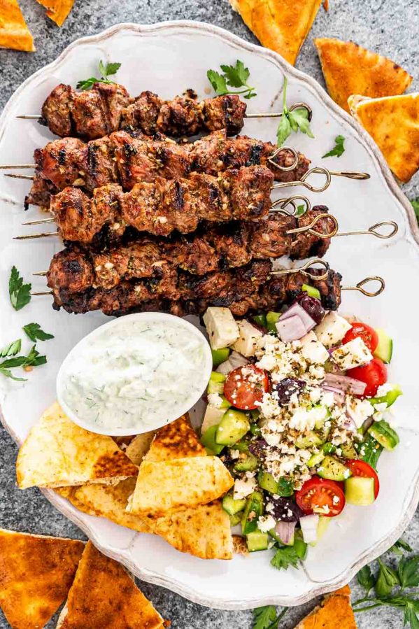 lamb souvlaki on a platter with tzatziki sauce, greek salad and pita bread.