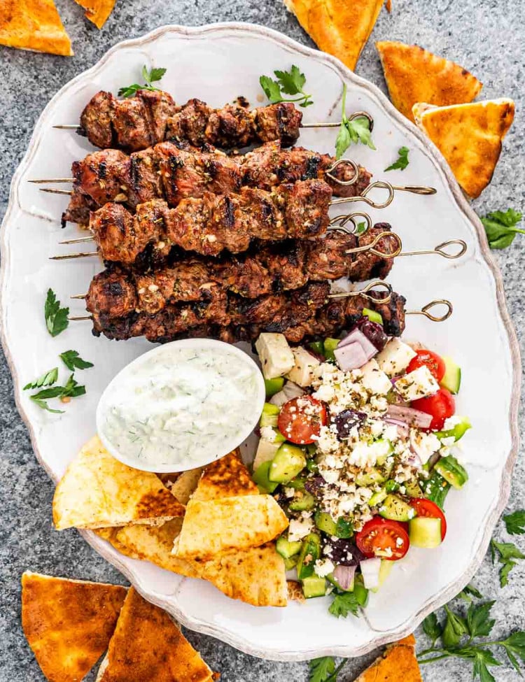 lamb souvlaki on a platter with tzatziki sauce, greek salad and pita bread.