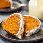 two slices of tomato cake with cream cheese icing on a plate with a glass of milk in the background.