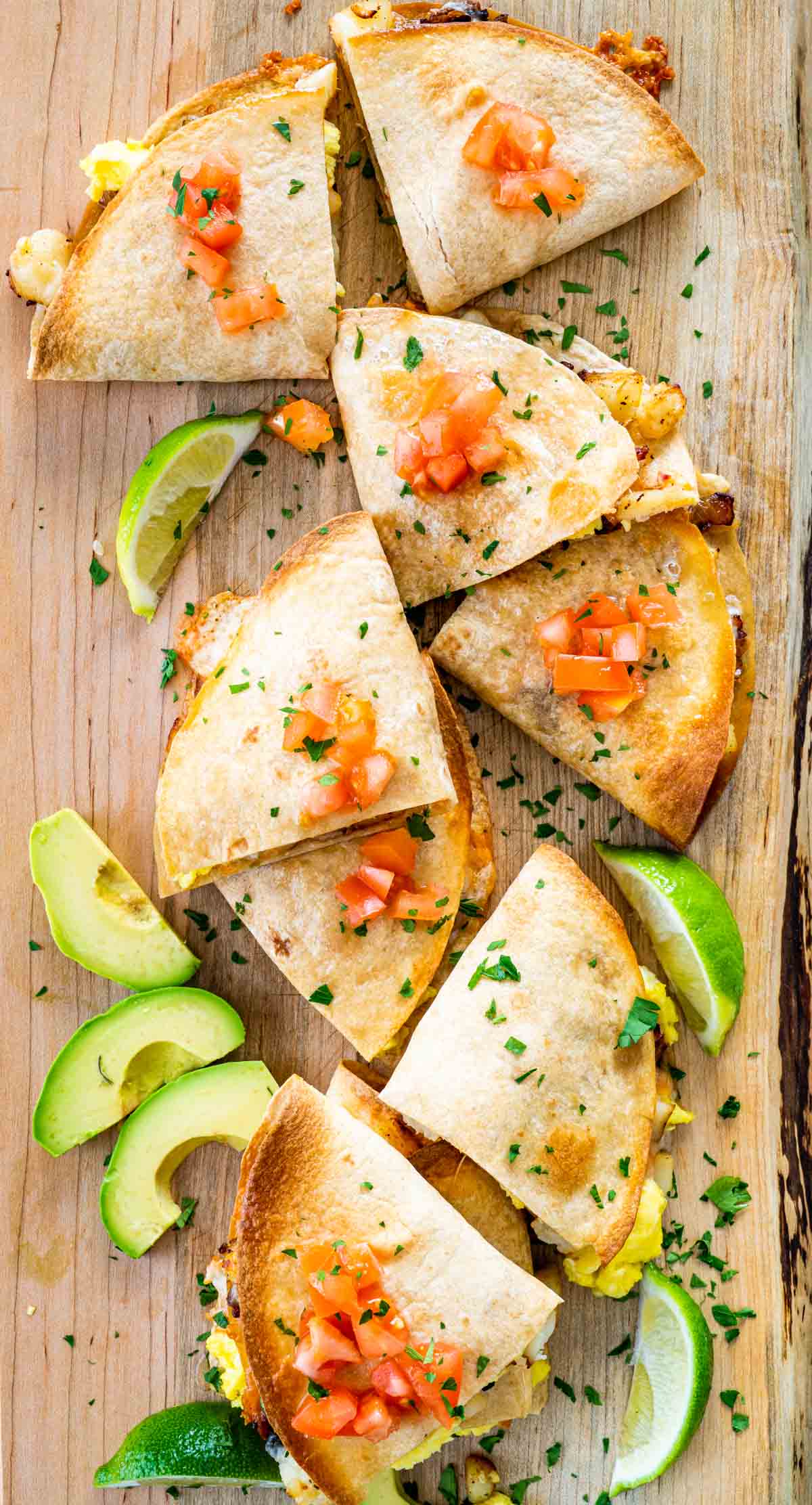 breakfast quesadillas cut in pieces on a cutting board garnished with tomatoes and avocados.