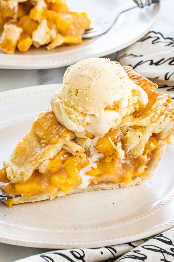 a slice of peach pie topped with a scoop of vanilla ice cream on a plate