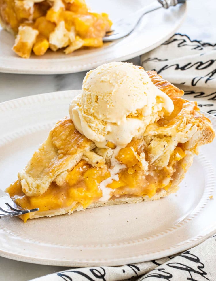 a slice of peach pie topped with a scoop of vanilla ice cream on a plate