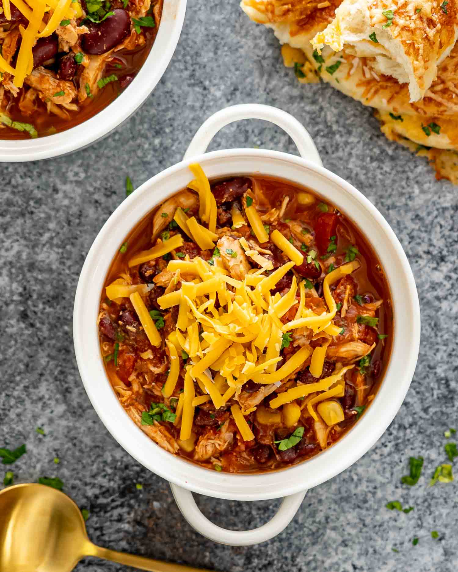 slow cooker chicken chili in a white bowl with some shredded cheddar cheese over the top.