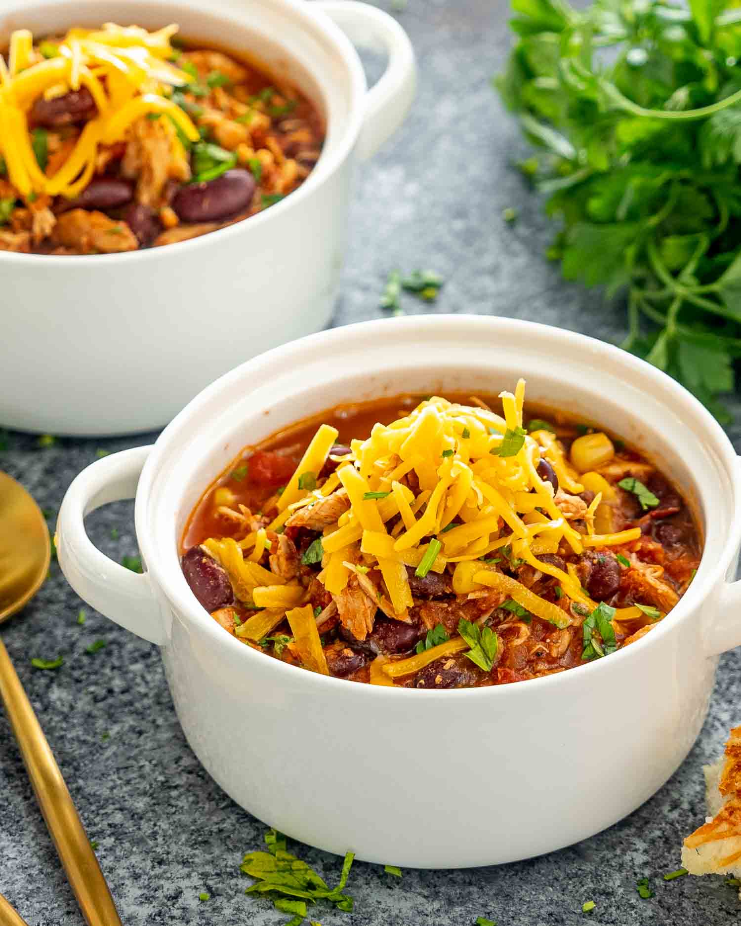 slow cooker chicken chili in a white bowl with some shredded cheddar cheese over the top.