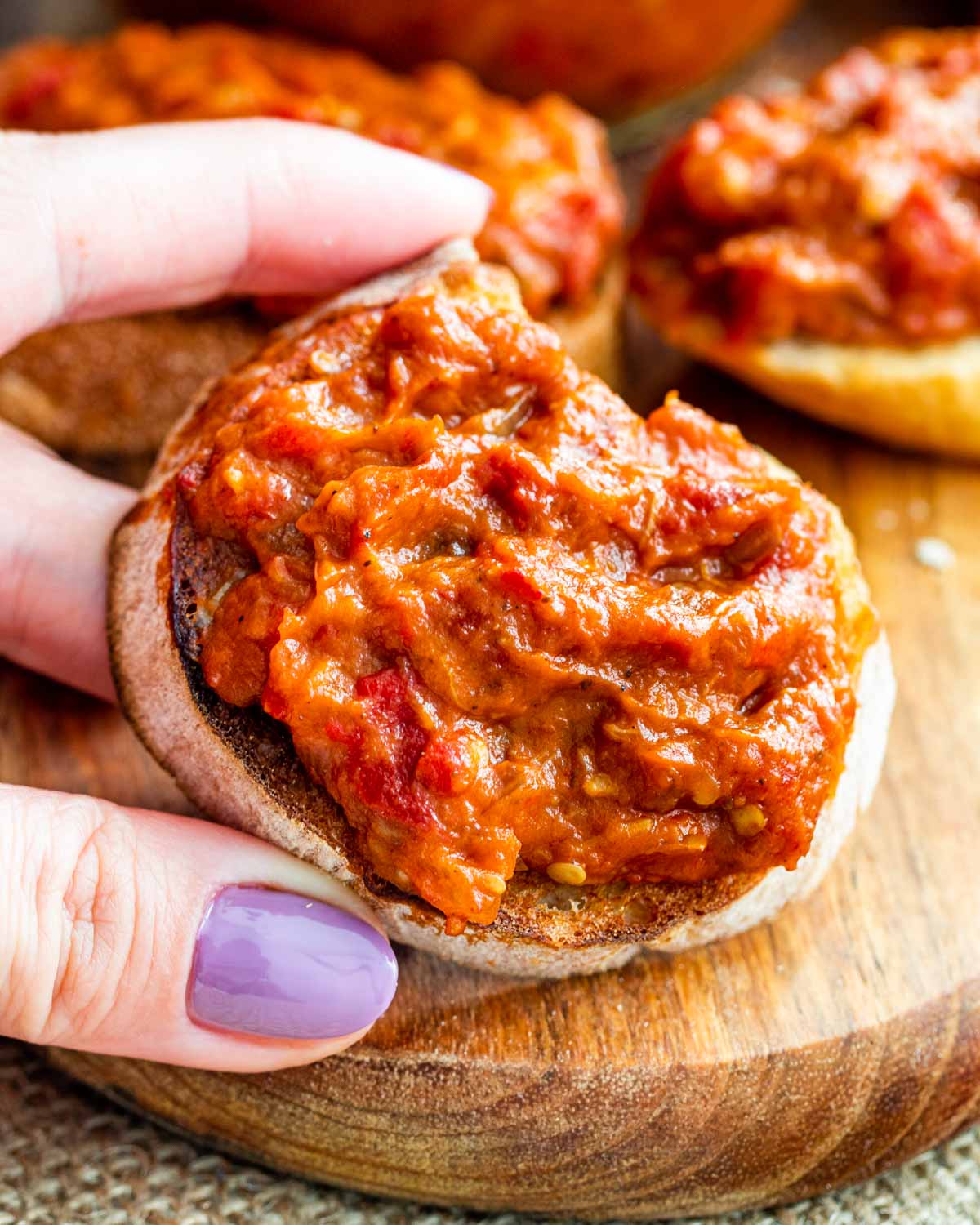 a hand holding a slice of bread with  roasted eggplant and pepper spread