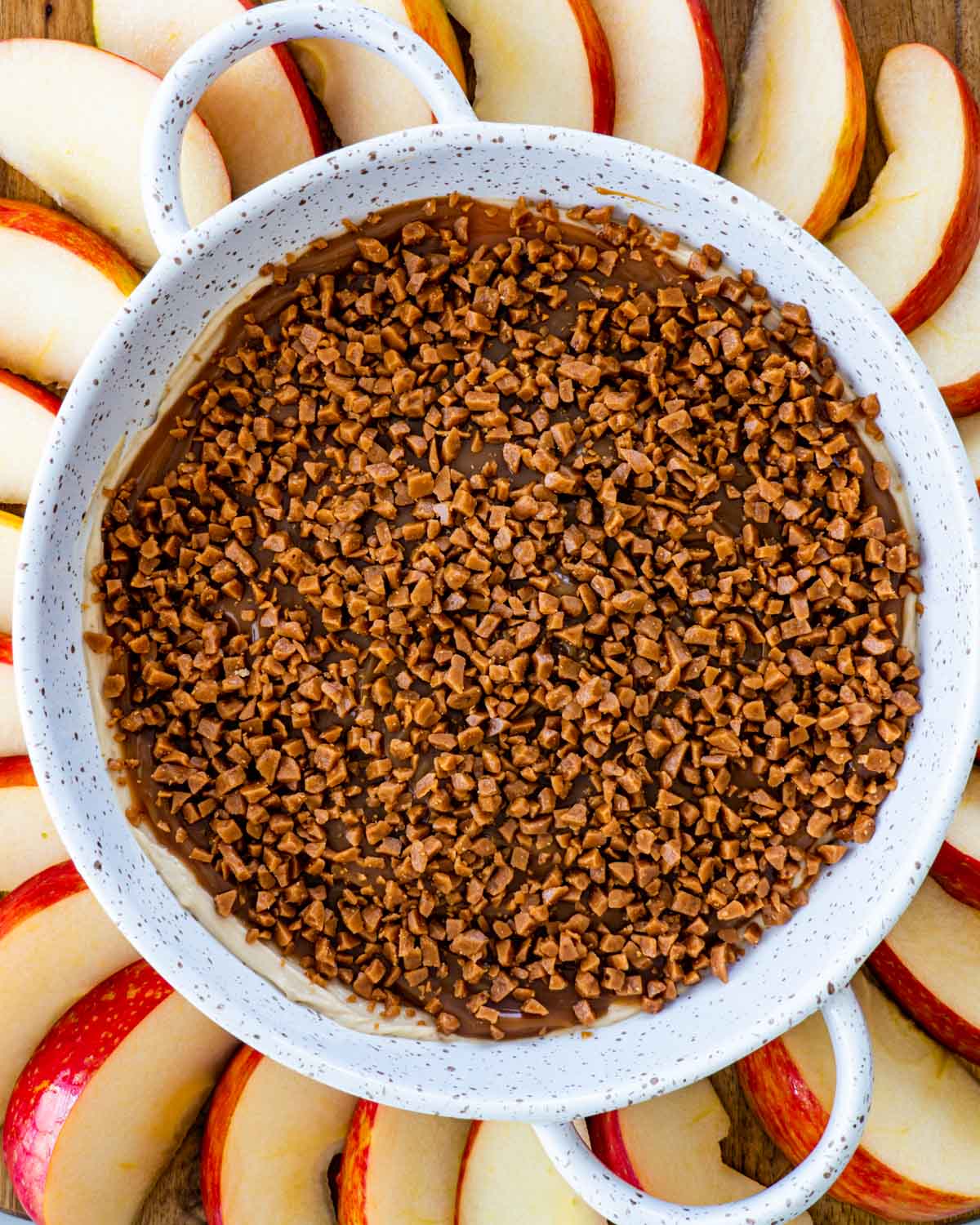 overhead shot of caramel apple dip in a round plate surrounded by apple wedges