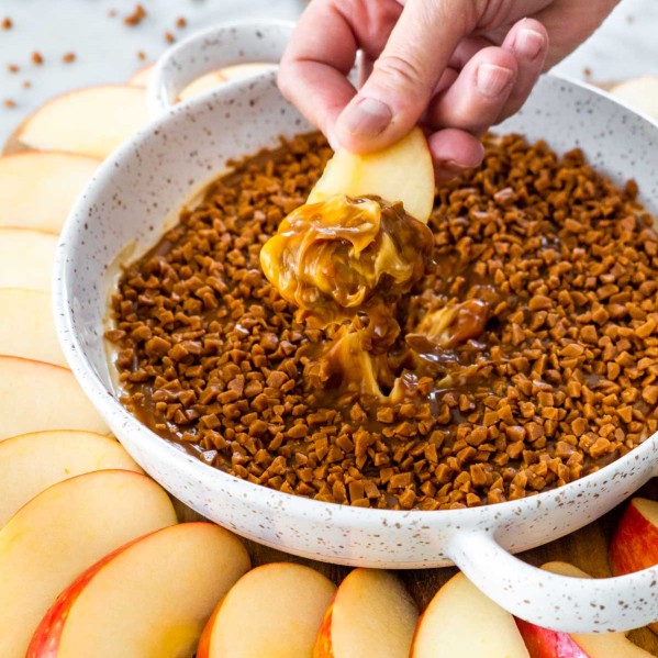 sideview shot of a hand dipping an apple wedge in caramel apple dip
