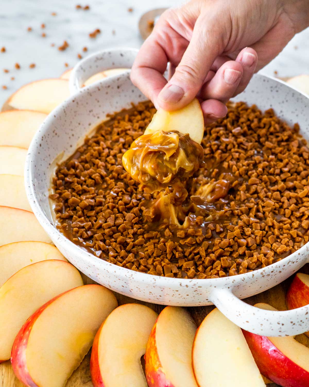 sideview shot of a hand dipping an apple wedge in caramel apple dip