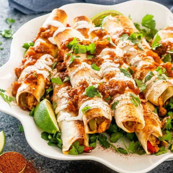 chicken fajita taquitos with sour cream and salsa on a white platter.