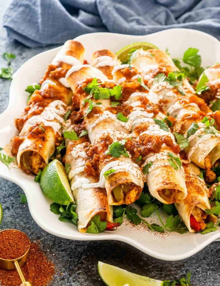 chicken fajita taquitos with sour cream and salsa on a white platter.