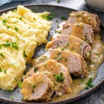 sliced cuban style pork tenderloin on a plate with mashed potatoes and gravy.