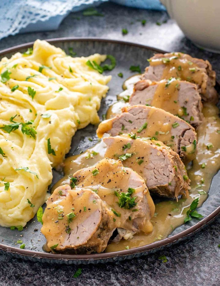 sliced cuban style pork tenderloin on a plate with mashed potatoes and gravy.