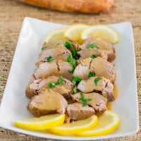 crockpot cuban style pork tenderloin, sliced and covered in sauce on a plate with slices of lemon