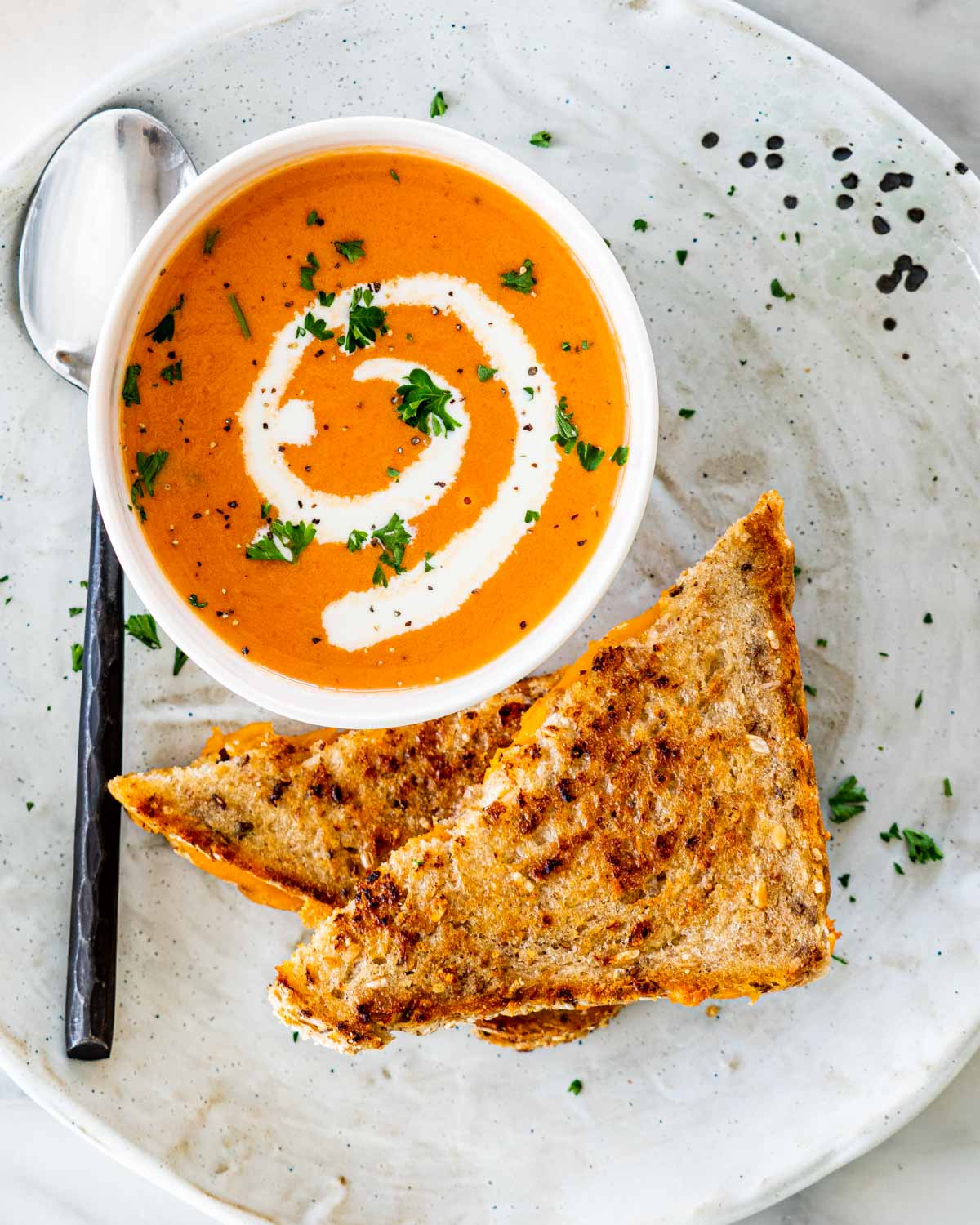 overhead shot of tomato bisque in a bowl with a garnish of heavy cream and a grilled cheese sandwich