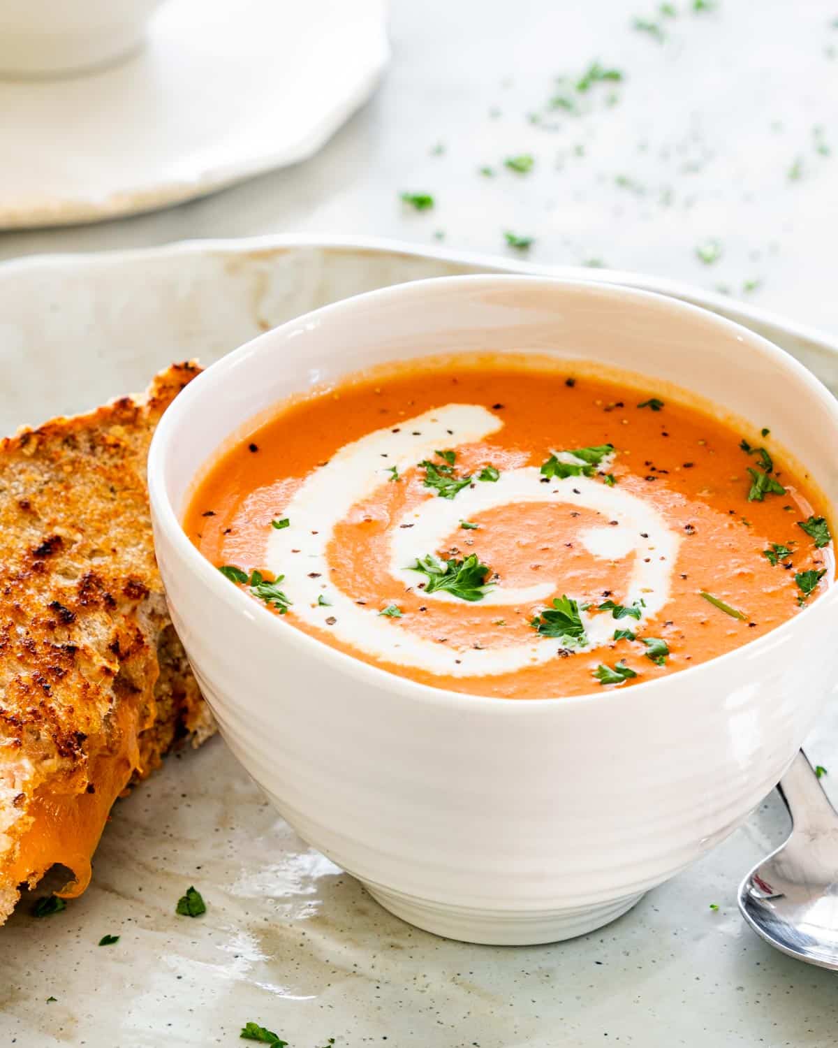side view shot of tomato bisque in a soup bowl with a grilled cheese sandwich