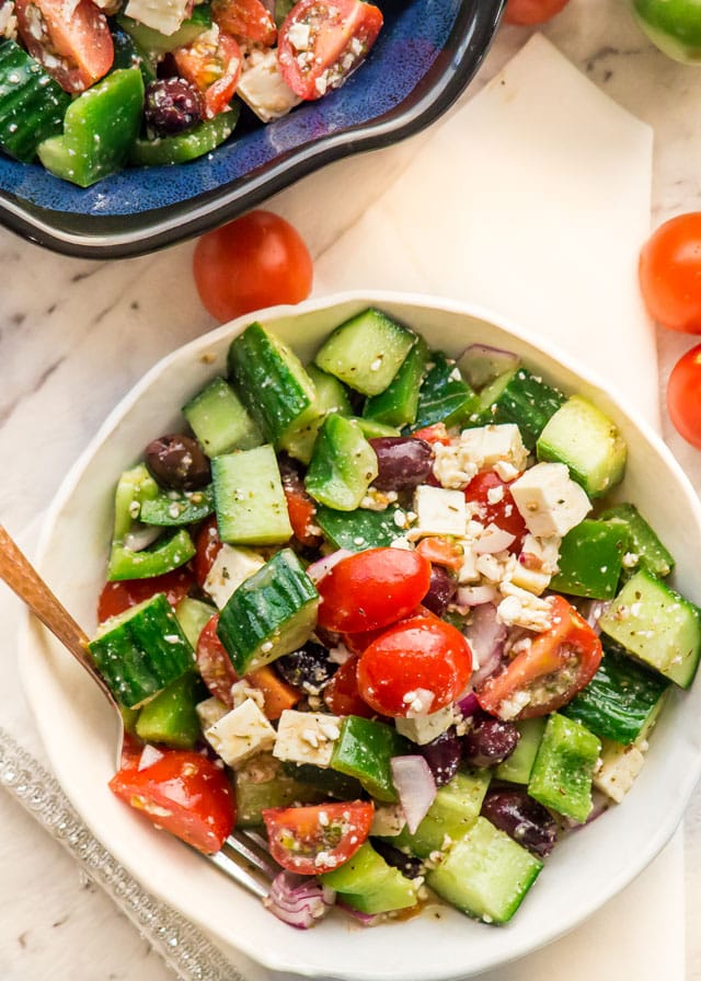 A white bowl filled with greek salad with cut tomatoes in the background