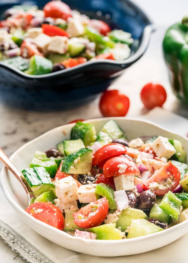 side view shot of greek salad in a white bowl with a bigger bowl in the background