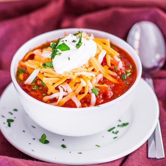 Healthier Beef Chili in a bowl topped with a dollop of sour cream and shredded cheese
