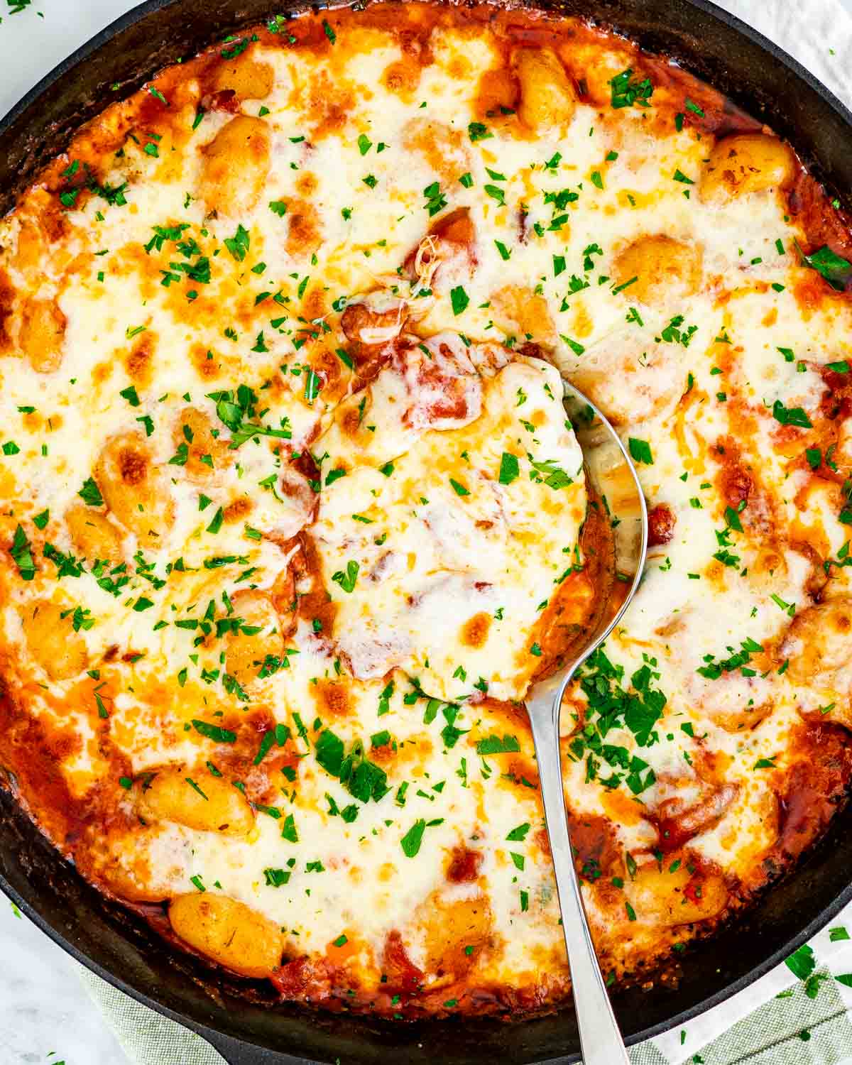 a black skillet with cheesy gnocchi bake and a serving spoon inside fresh out of the oven