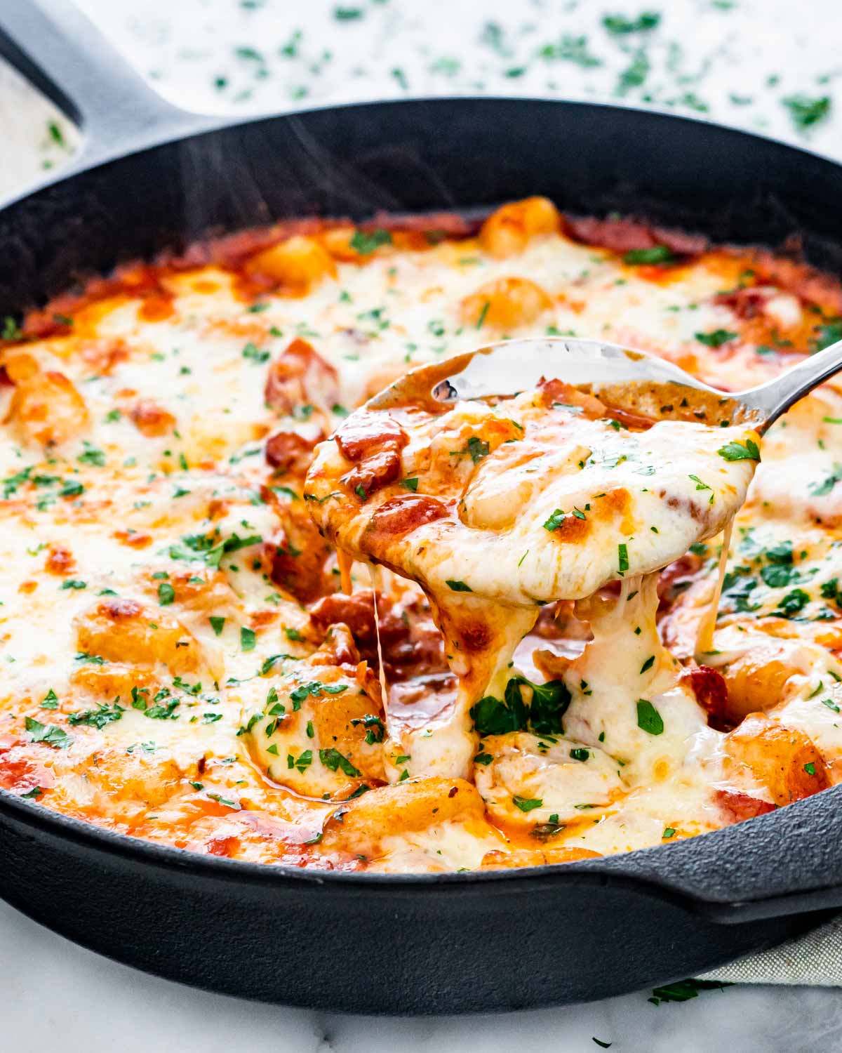 a serving spoon scooping out a healthy portion of cheesy gnocchi bake from a skillet