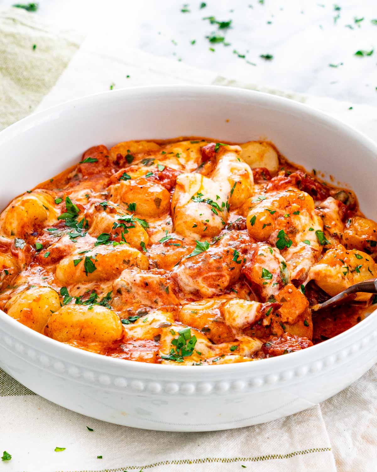 a white plate loaded with glorious cheesy gnocchi in a tomato bacon sauce