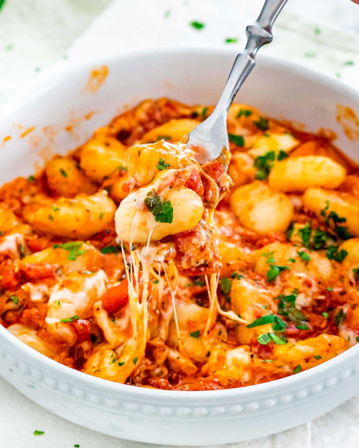 a fork holding gnocchi in sauce over a plate loaded with cheesy gnocchi bake