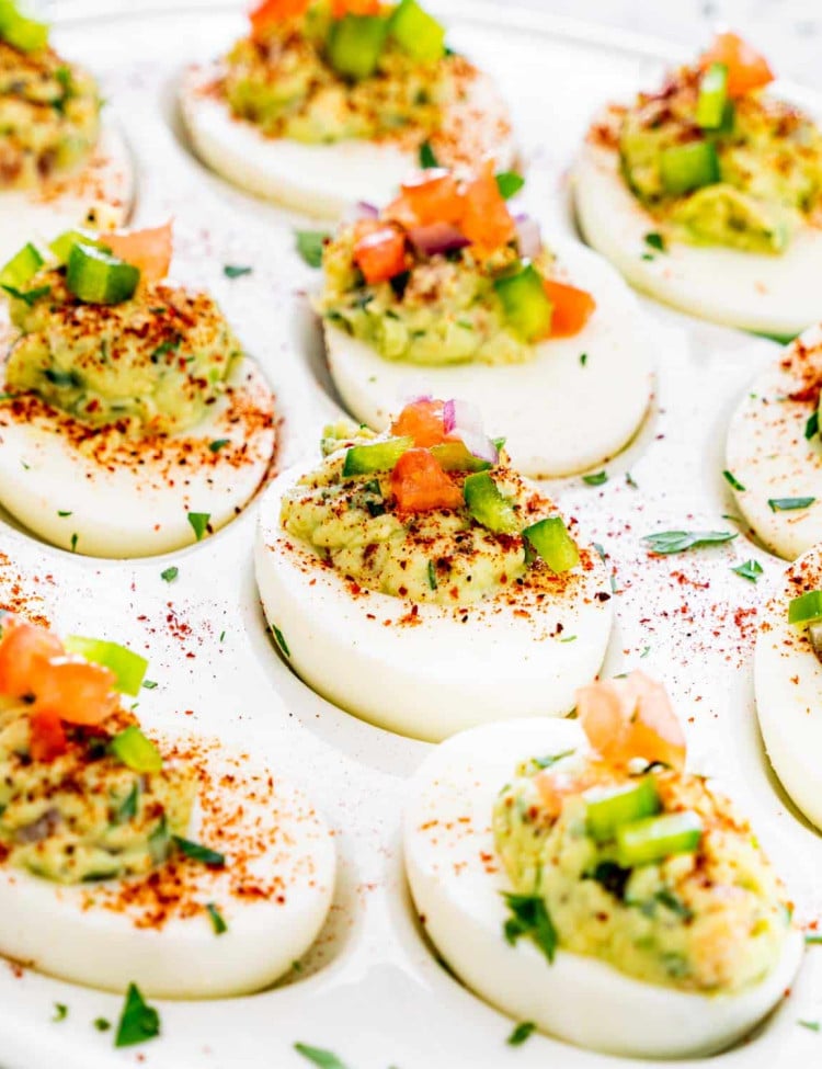 close up side view shot of guacamole deviled eggs lined up on a plate