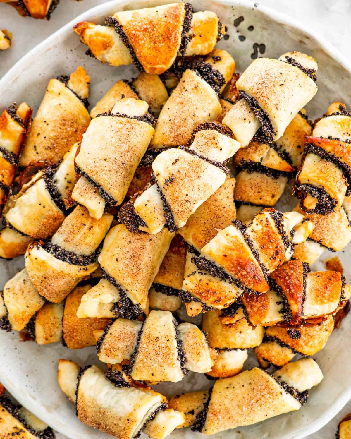 overhead shot of a bunch of poppy seed rugelach cookies on a plate.