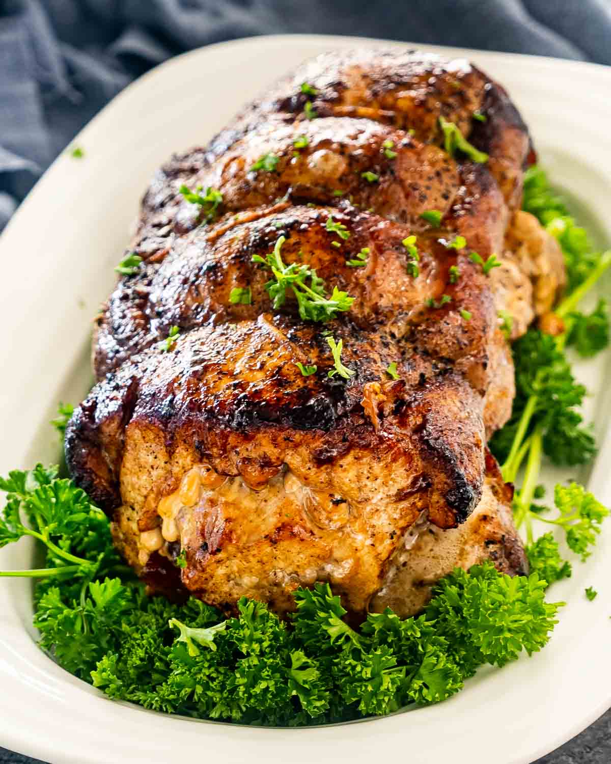 apple stuffed pork loin on a white platter with parsley.