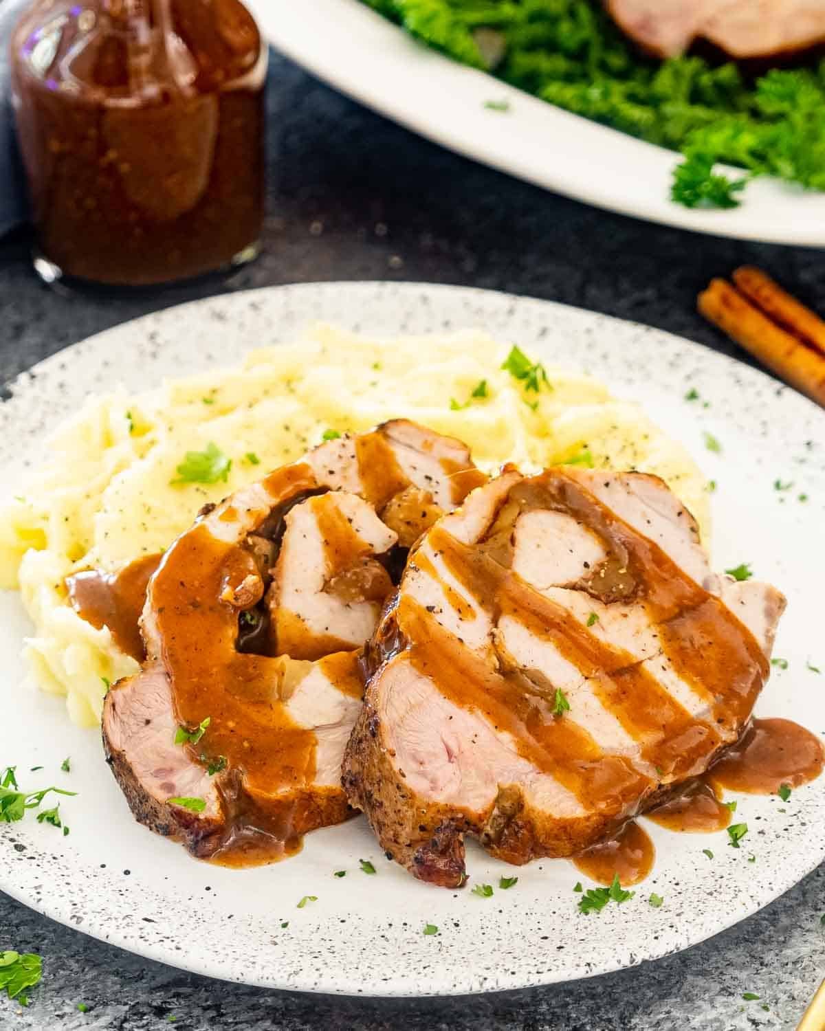 2 slices of apple stuffed pork loin with mashed potatoes on a plate.