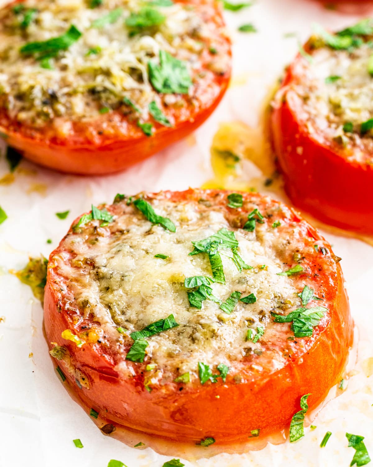 side view shot of 3 slices of baked parmesan tomatoes garnished with parsley