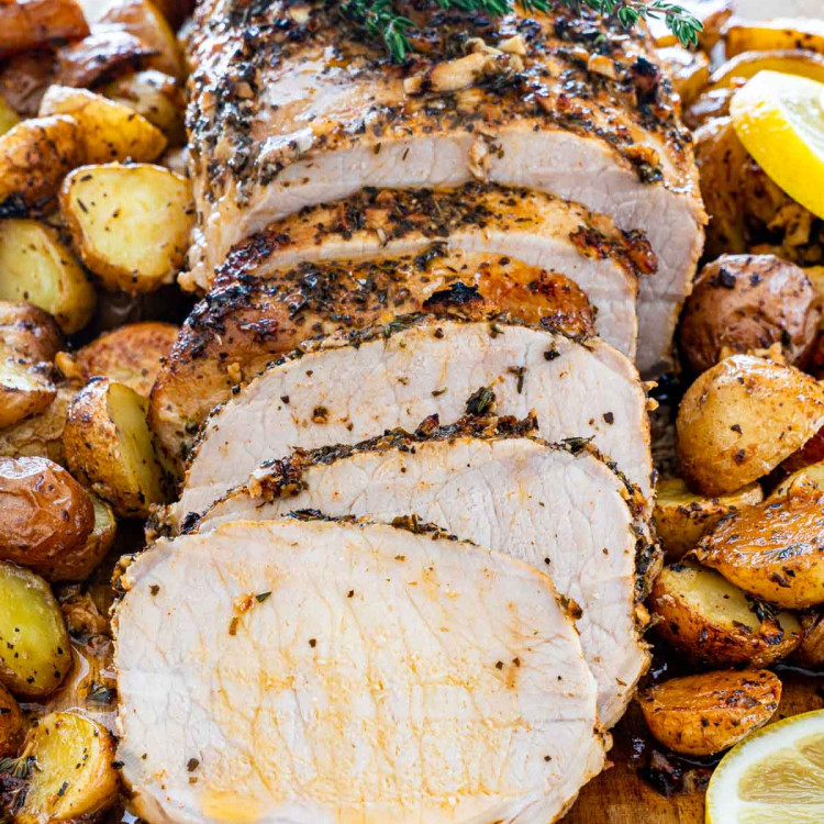 Sliced lemon garlic pork roast topped with a sprig of thyme, surrounded by roasted potatoes