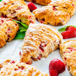 a bunch of strawberry scones drizzled with lemon icing on a piece of parchment paper, with scattered strawberries and mint