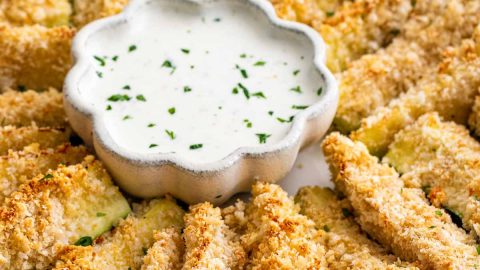 baked parmesan zucchini sticks on a serving platter with a bowl of ranch dressing.