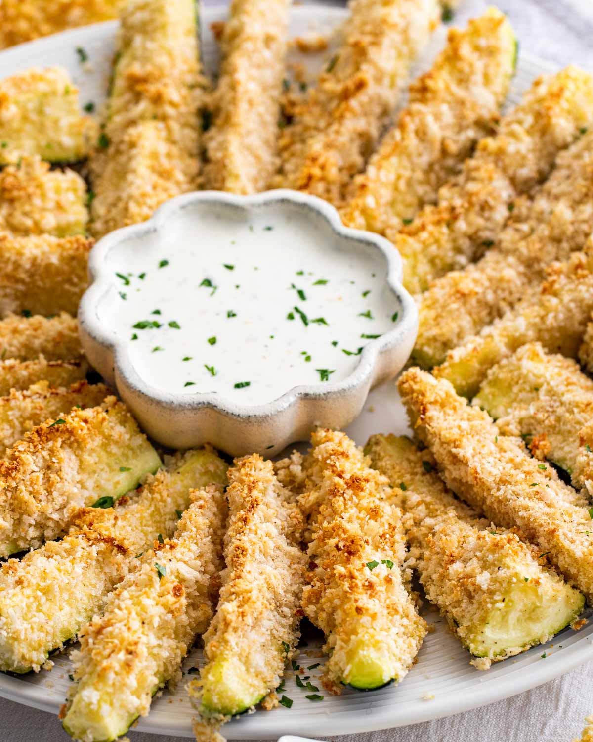 baked parmesan zucchini sticks on a serving platter with a bowl of ranch dressing.